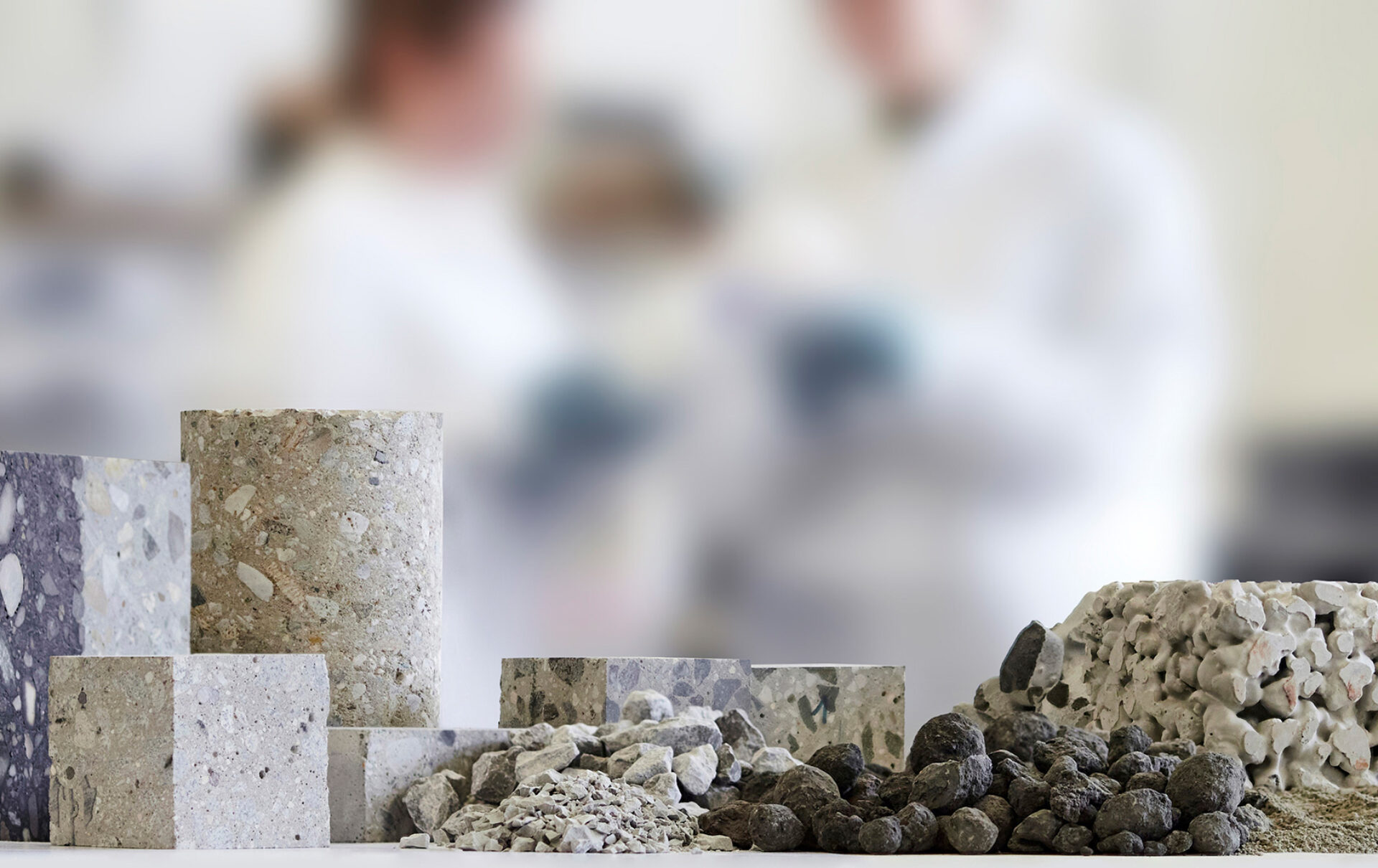 Betonproben im Vordergrund, Forscherinnen im Labormantel im Hintergrund