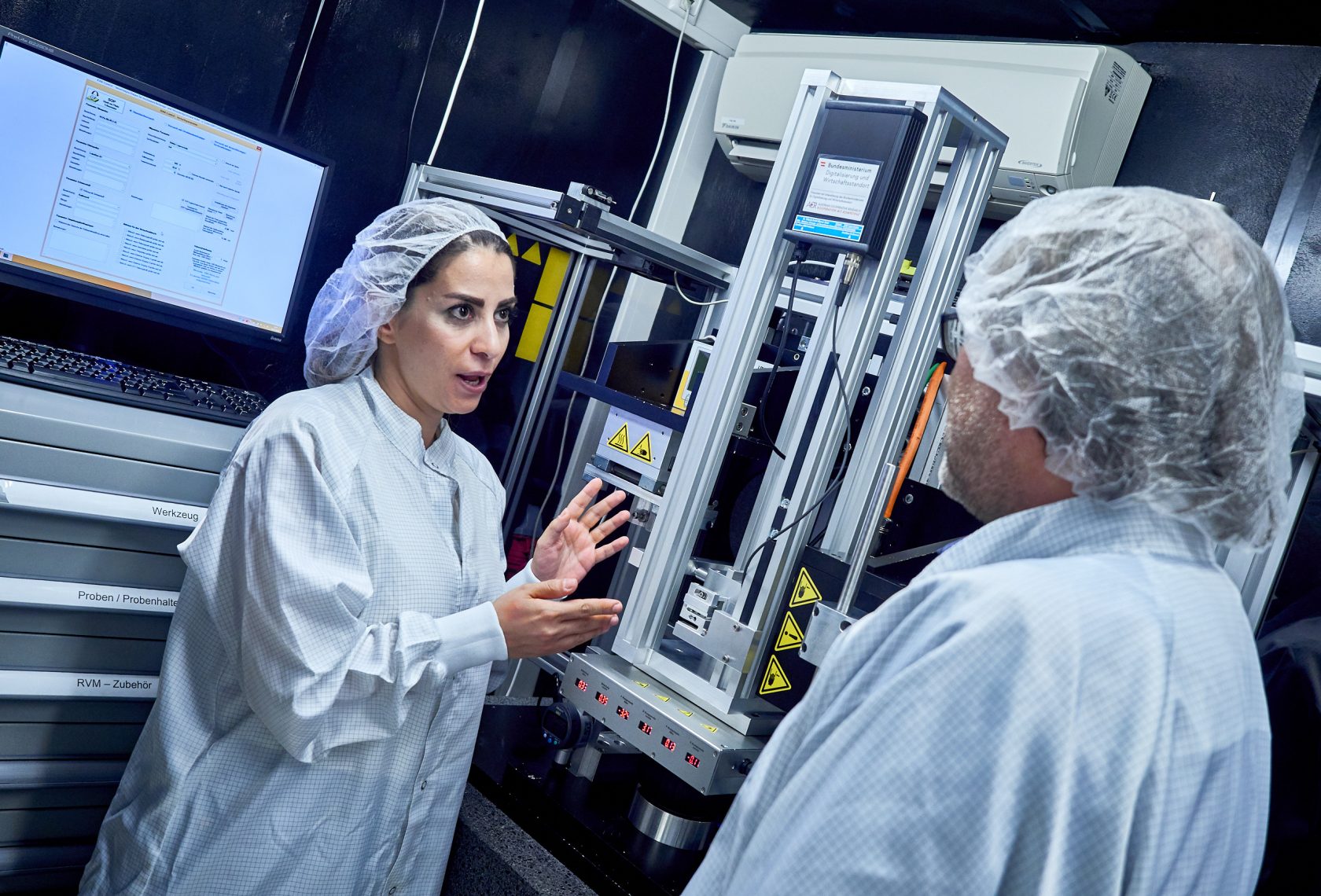 Forscherin und Forscher im weißen Kittel vor einem Gerät für Reibungsversuche