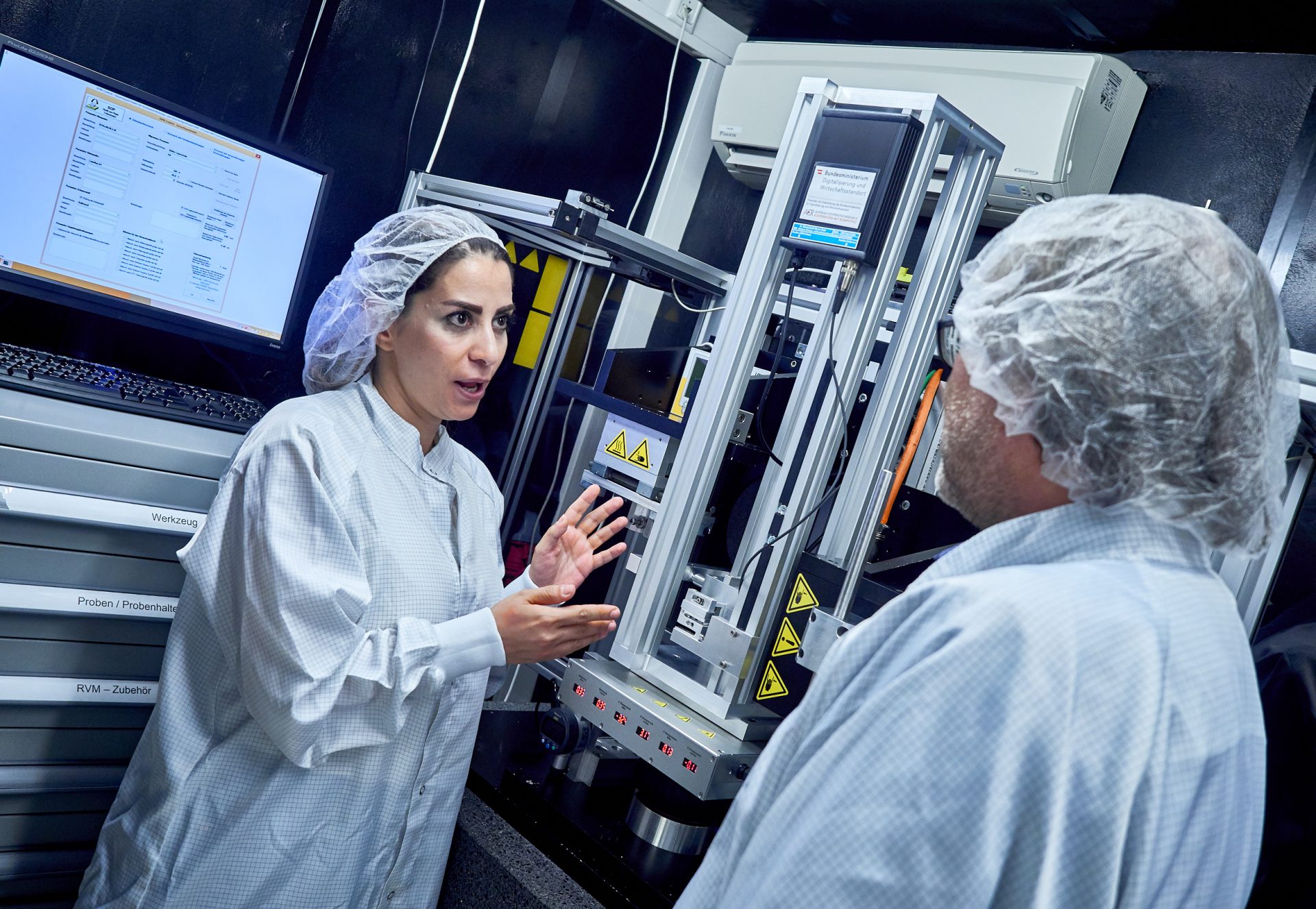 Forscherin und Forscher im weißen Kittel vor einem Gerät für Reibungsversuche