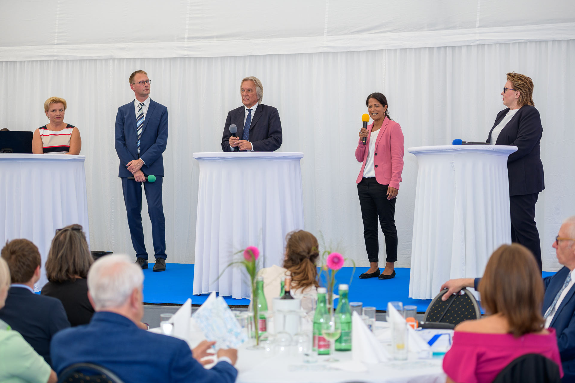 Fünf Personen am Podium bei einem Podiumsgespräch, im Vordergrund Teile des Publikums