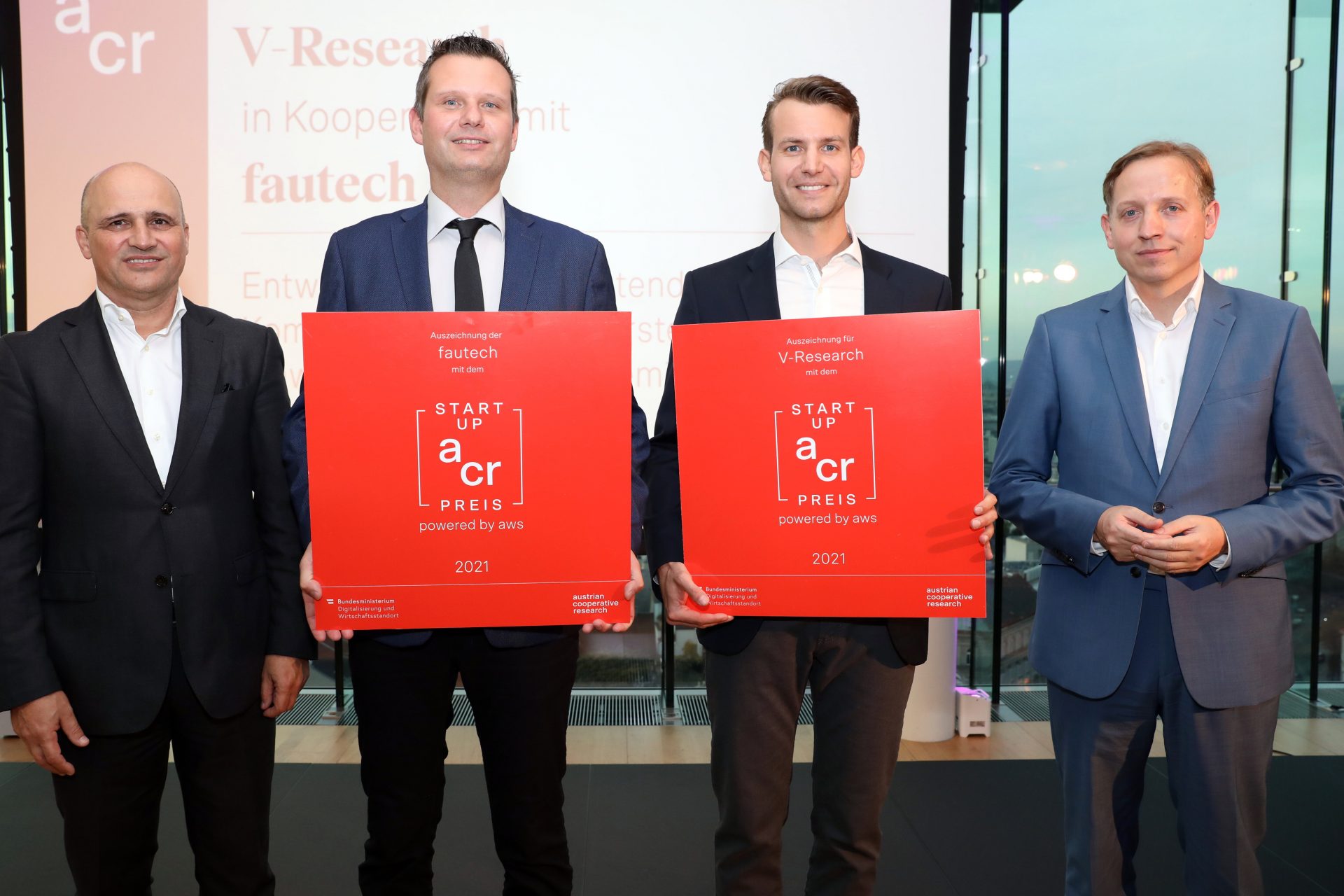 Vier Personen auf der Bühne, zwei in der Mitte halten große rote Schilder in der Hand