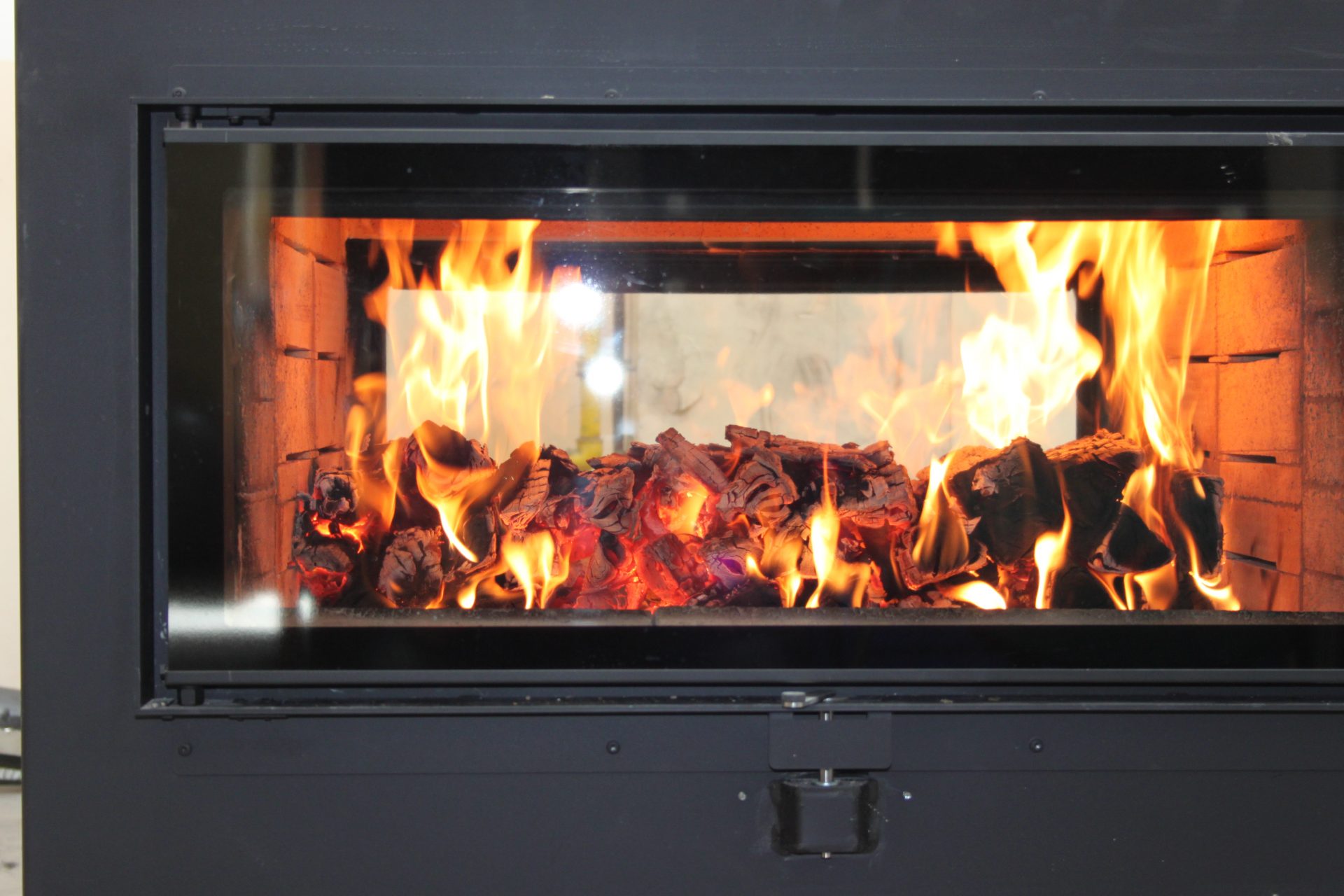 Blick durch das Kachelofenfenster auf brennendes Holz
