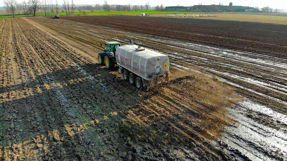 Traktor mit Anhänger verteilt Düngemittel auf dem Feld