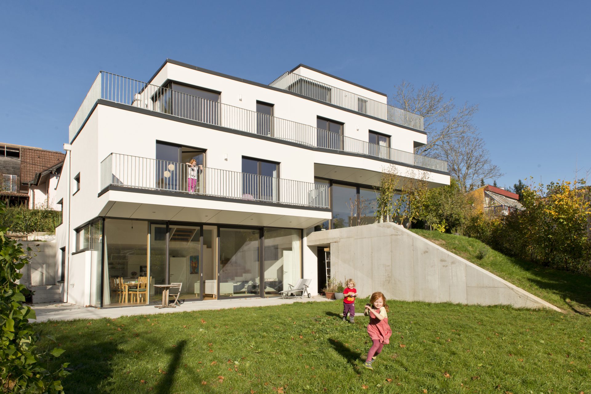 Mehrstöckiges Wohnhaus mit Garten davor und spielenden Kindern