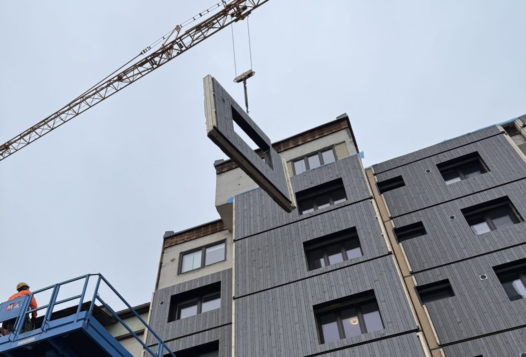 Gebäude im Hintergrund, Baukran mit Fassadenelement im Vordergrund
